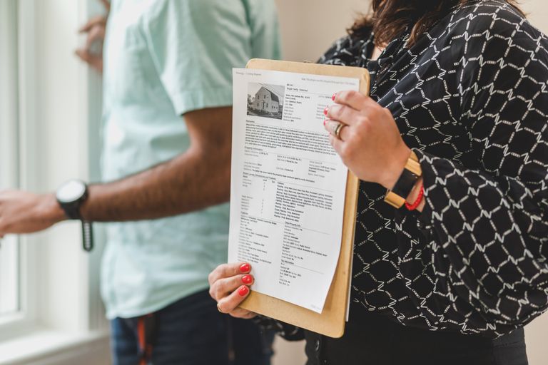 Real estate agent holding property documents on a clipboard in an office setting.